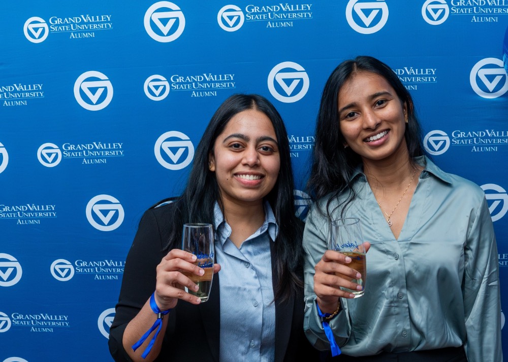 two girls smile in front of the GVSU Alumni backdrop